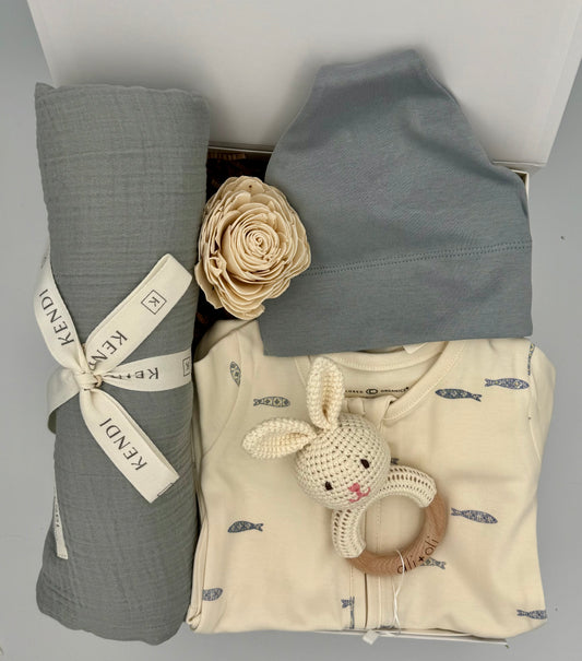Baby clothing and用品 including a gray swaddle, blue hat, and beige outfit with a toy on a light gray background.