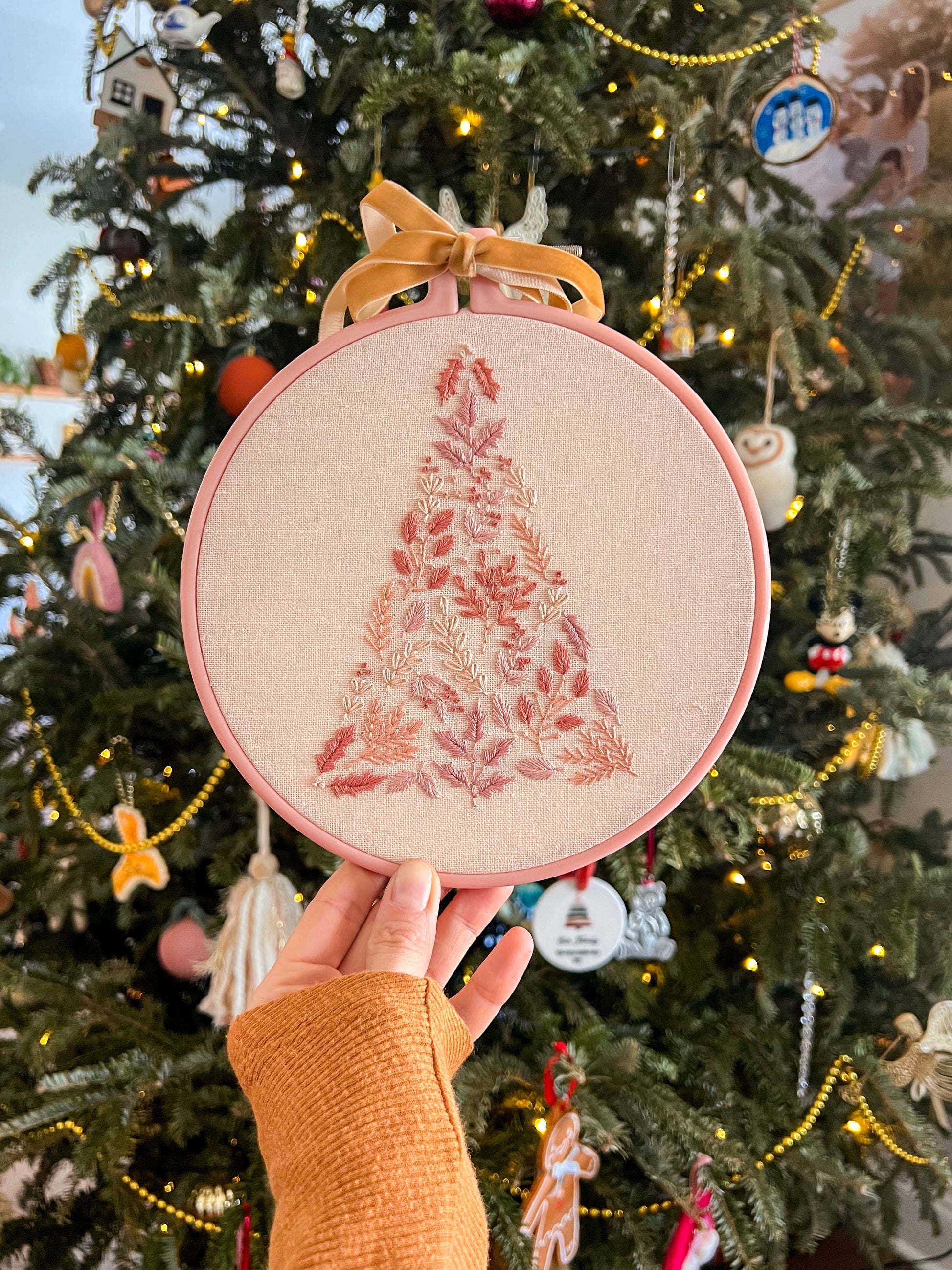 Hand holding a embroidery hoop with a floral design in front of a decorated Christmas tree.