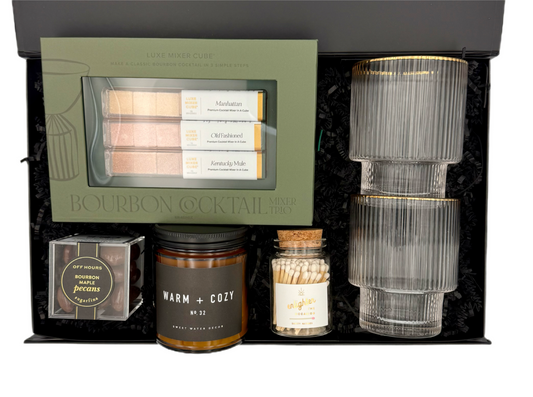 Gourmet gift set with bourbon cocktail mix, candles, and decorative items in a black box.